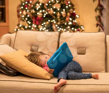 Young girl lying at home on settee and using a child's tablet touch screen computer at xmas suggesting this was a present
