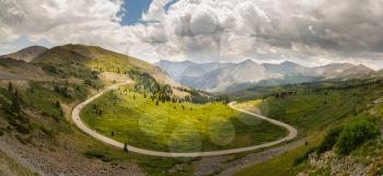 Panorama of wide curving bend on road climbing to top of Cottonwood Pass in Colorado as sports cars race to summit