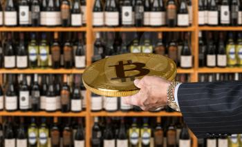 Businessman offering a bitcoin in payment for bottles of wine in wine store or supermarket in concept for e-commerce