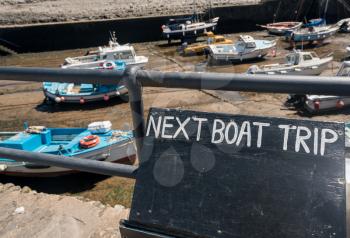 Boats beached in the mud in harbor as a sign announces next boat trip
