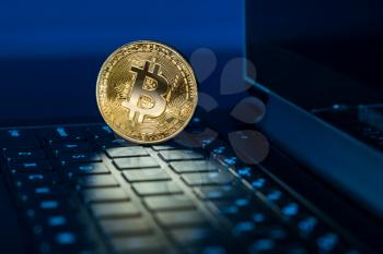 Single bitcoin coin standing on the keyboard of modern laptop computer