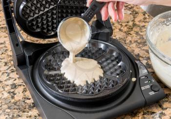 Batter being poured into norwegian heart shaped waffle maker on granite kitchen worktop