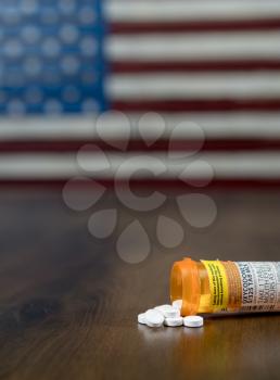 Oxycodone is the generic name for a range of opoid pain killing tablets. Prescription bottle for Oxycodone tablets and pills on wooden table with USA flag in background