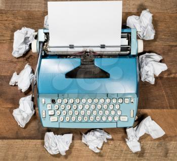 Modern electric typewriter on wooden desk background with papers ready for a new book or novel with many failed pages screwed up on desktop