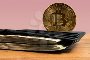 Bitcoin coin standing behind leather wallet stuffed with US dollar bills