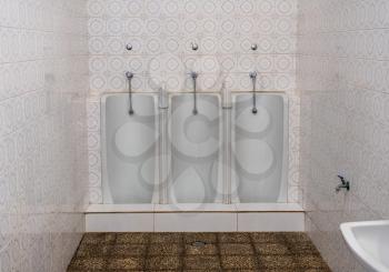 Set of three side by side full length mens urinals in porcelain against a tiled wall in small restroom