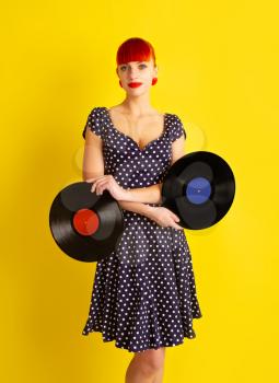 Pretty girl in retro dress in polka dot holding vinyl discs on a bright yellow background