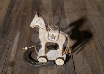 Wooden children's toy horse on wheels and a real steel horseshoe on a dark background of boards