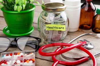 Saving money for health care insurance - money glass, stethoscope, pills and bottles