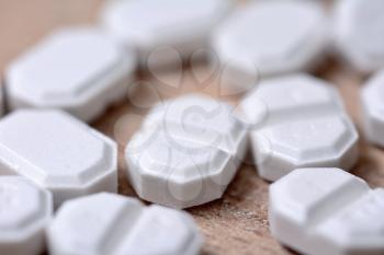 Macro of the white pills on wooden brown background.