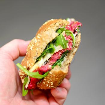 Mans Hand Holding a Beetroot and Arugula Burger with Missing Bites.