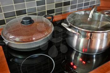 Black kitchen induction stove with stainless steel pot and pan. Cooking in pots on kitchen stove with modern tiling.