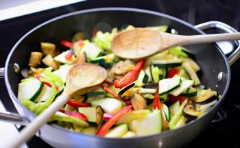 Stir fry fresh chopped eggplant, zucchini and peppers in the pan with wooden spoon. Preparing healthy food.