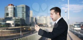 Businessman Holding Smartphone in Hand And Feeling Angry With Business City and Corporate Buildings In Background