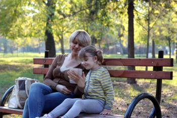 mother and daughter sitting in park and play with tablet