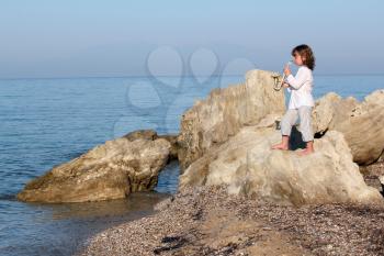 little girl standing on a rock by the sea and playing saxophone