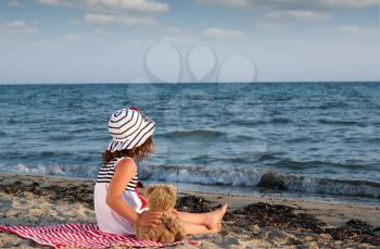 little girl with teddy bear sitting on beach
