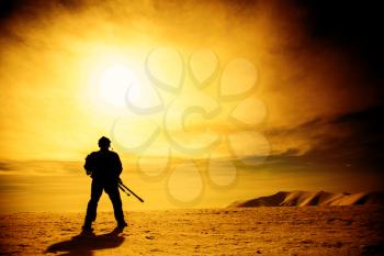 Silhouette of soldier with sniper rifle standing under scorching sun in the mountains