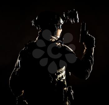 Army elite forces soldier, police special operation, counter terrorist team member in tactical ammunition with hidden behind mask identity, standing backwards with pistol in hand, low key studio shoot