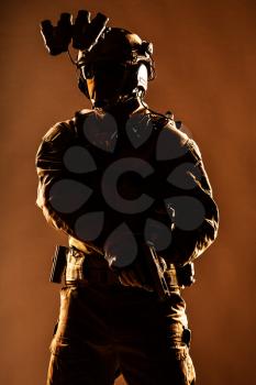 Anti terrorist squad fighter, army elite forces soldier in mask, with night vision device and tactical radio headset on helmet, armed service pistol standing ready for action, low key studio shoot