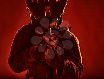 Special operations forces soldier, counter terrorism assault team fighter with night vision device on helmet and red dot laser sight on service rifle, low key studio shoot silhouette with backlight