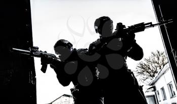 Silhouettes of police special operations forces tactical team, SWAT fighters aiming assault rifles while standing shoulder to shoulder in bright white doorway. Military tactical group storming room