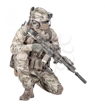 Army special forces infantry in battle uniform, radio headset on helmet, armed service rifle, standing on knee, waiting in ambush, patrolling area, observing territory studio shoot isolated on white