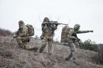 Army team members, military mercenary group in various types camouflage uniform, armed service rifles, observing territory from hill, patrolling area during mission