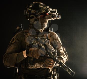 Army special forces tactical group fighter moving in darkness, using radio headset, looking through four lens night-vision, thermal imaging device on helmet, armed small submachine gun with silencer