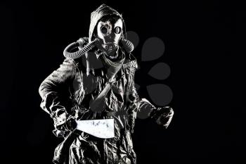 Low key portrait of post apocalyptic creature, living in catacombs mutant, survived in nuclear disaster human in ragged cloth and gas mask, armed with handmade cold weapon isolated on black background