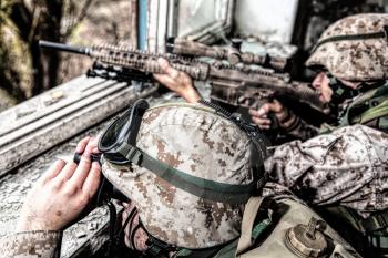 Marines sniper team armed with large caliber, anti-materiel sniper rifle hiding in ruined urban building, shooting enemy targets on range from shelter, sitting in ambush. Military firefight in city