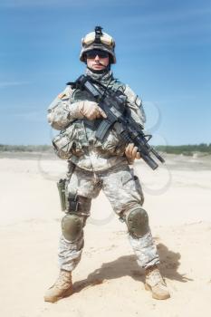 Portrait of United states airborne infantry corporal with arms, camo uniforms dress. Combat helmet on, tactical light, boots and kneepads, front view