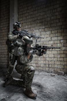 Pair of US Army Rangers with machinegun and rifle moving along the wall after each other on military mission