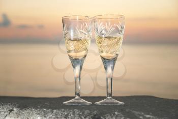 Two wedding glasses with champagne over sunset