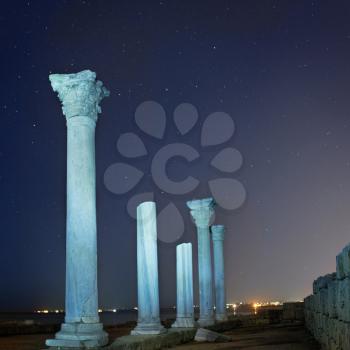 Ruins of ancient city columns under blue night sky with moon and stars