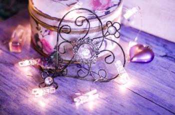 Vintage metal heart with a crystal on a background of violet drapery with lights of the garland. Mysterious Valentine's Day Concept.