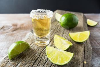 Tequila shot with lime on rustic wooden background. Strong alcohol  drink. Gold Mexican tequila shot. 