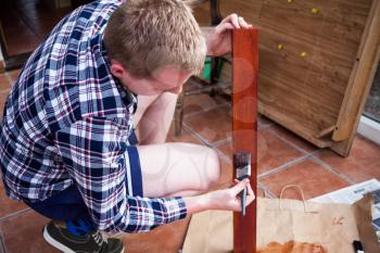 Housekeeper paints wooden boards with paintbrush. Home improvements and renovations concept. Young man holds brush in hands. Painting old wooden furniture