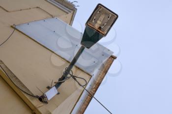 Rusty old hanging lamp post with wires in it. Placed above the light collored wall outside the building. Aging but light is still working and functional. 