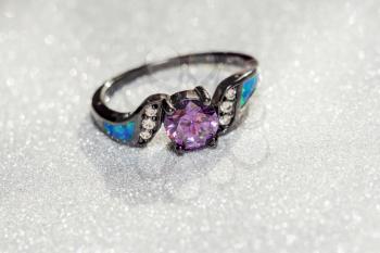 Fashion black gold ring with purple amethyst on glittering background.