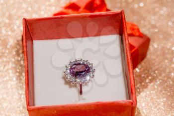 Silver amethyst ring in a red gift box on glittering background.