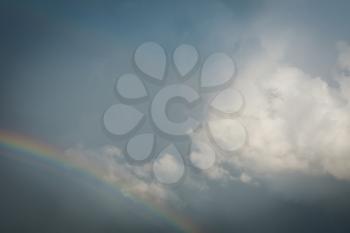 Dark rain clouds and colorful rainbow in the sky background.