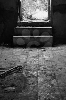 Broken door frame and debris on dirty tiled floor of an abandoned house. Black and white.