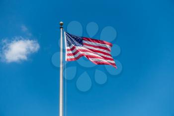 A photo of the American flag on a long pole with blue sky behind.