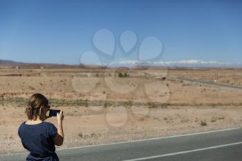 Girl taking picture of beautiful scenic road with blue sky and the High Atlas Mountains in Morocco, Africa