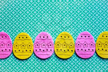 Decorated felt easter eggs yellow and pink on a green pattern background