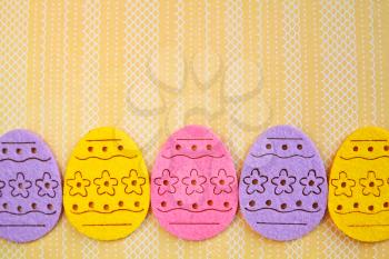 Decorated felt easter eggs yellow, pink and lilac on a yellow lined background