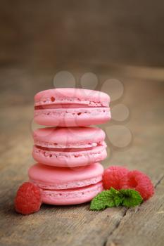 Row of three raspberry macarons on a wooden table with fresh fruits and mint