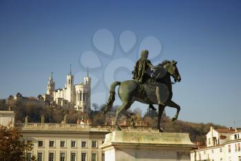 Louis XIV equestrian statue located at the center of the Bellecour square in Lyon, France.  Fourviere basilica in background.