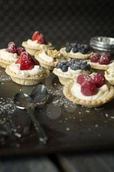 Blueberry, strawberry and pistachios tartlets with spoons on biscuit sheet on a wooden table